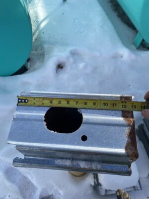 Galvanized 13-inch Westeel floor support measured with a tape measure outdoors on snow.