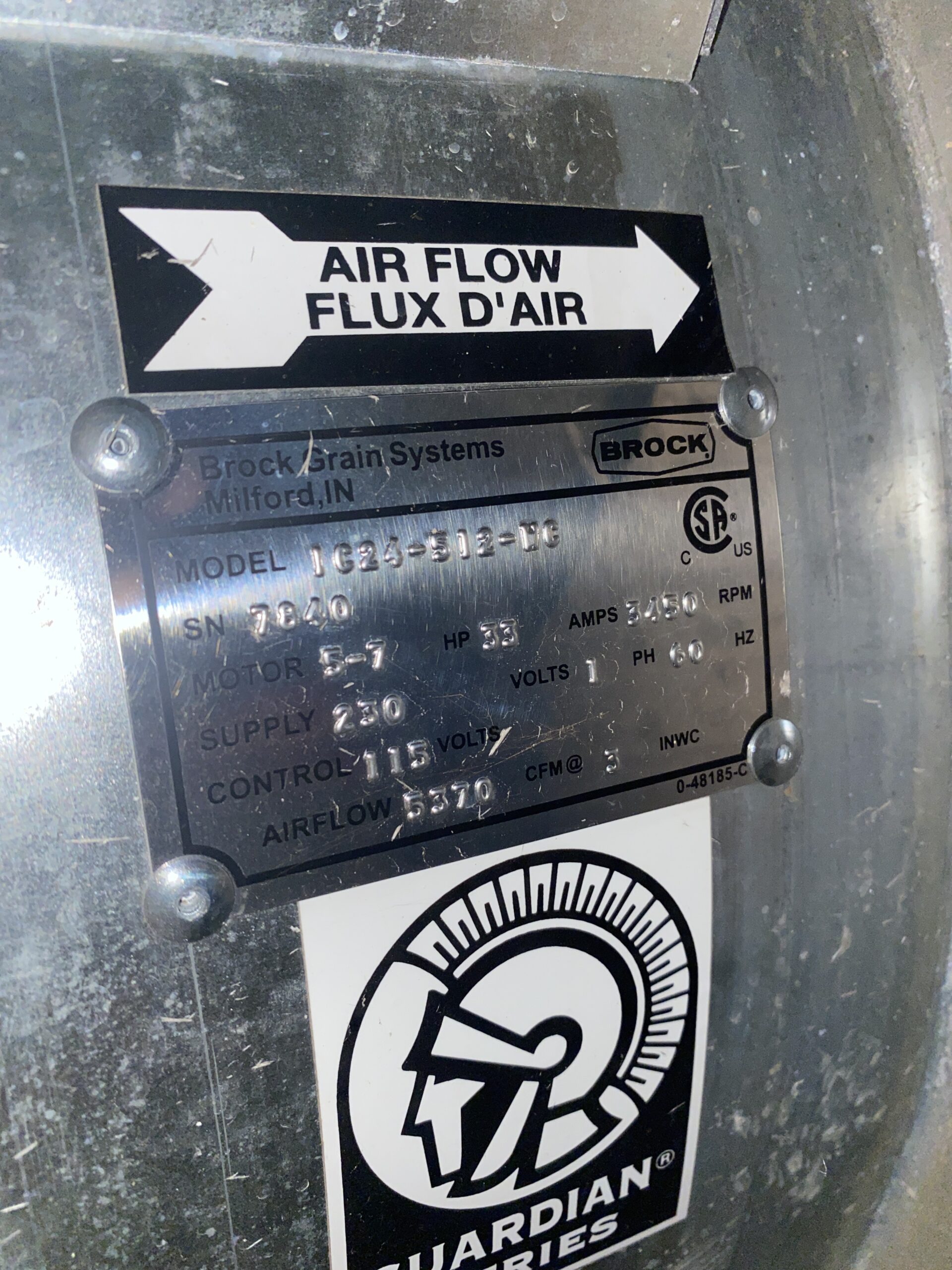 Close-up of Brock Grain Systems identification plate and airflow direction label on a galvanized grain bin fan