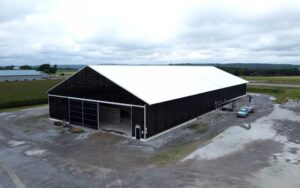 Large agricultural storage building with a white roof and dark steel siding, photographed from above on a rural property.