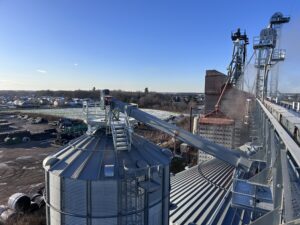 Grain bin with custom-engineered bin‑top platform and overhead conveyor system at an agricultural grain handling facility.