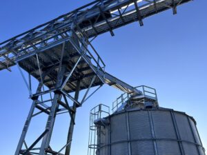 Steel grain handling structure with an elevated conveyor support system and a custom engineered platform installed on top of a grain bin.
