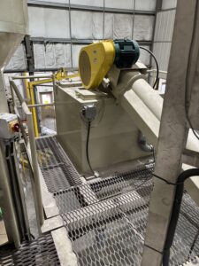 Industrial screw conveyor with motor and gearbox mounted on an elevated steel platform inside a bulk material handling facility.