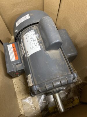 New US Motors 3HP farm duty motor resting inside a cardboard box, showing casing, labels, and shaft.