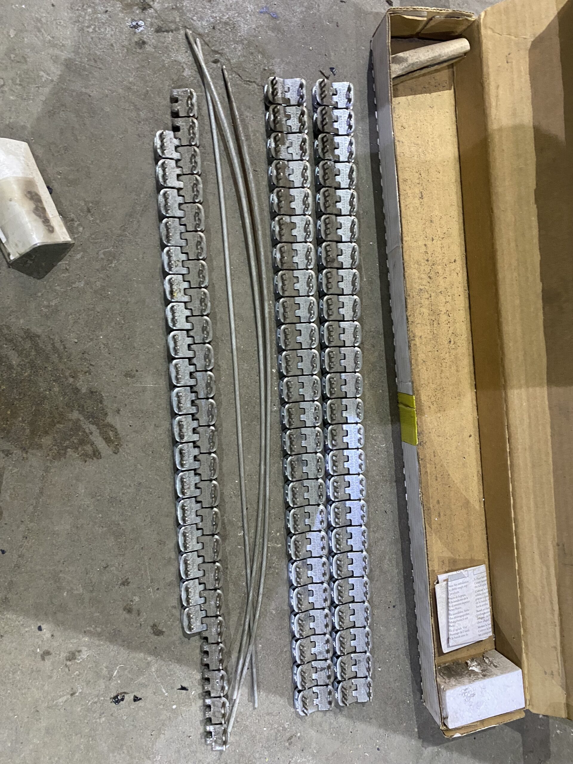Metal Alligator splice strips and hinge pins laid out on a shop floor next to an open cardboard box.