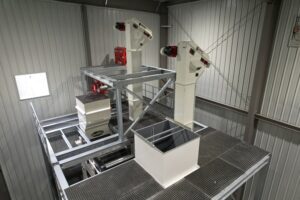Indoor bulk material handling installation featuring twin bucket elevator heads, steel support structure, and elevated grated platforms inside a processing facility.
