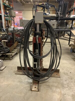 Hydraulic grain bin jack with coiled hydraulic hoses standing on a steel base in a workshop.