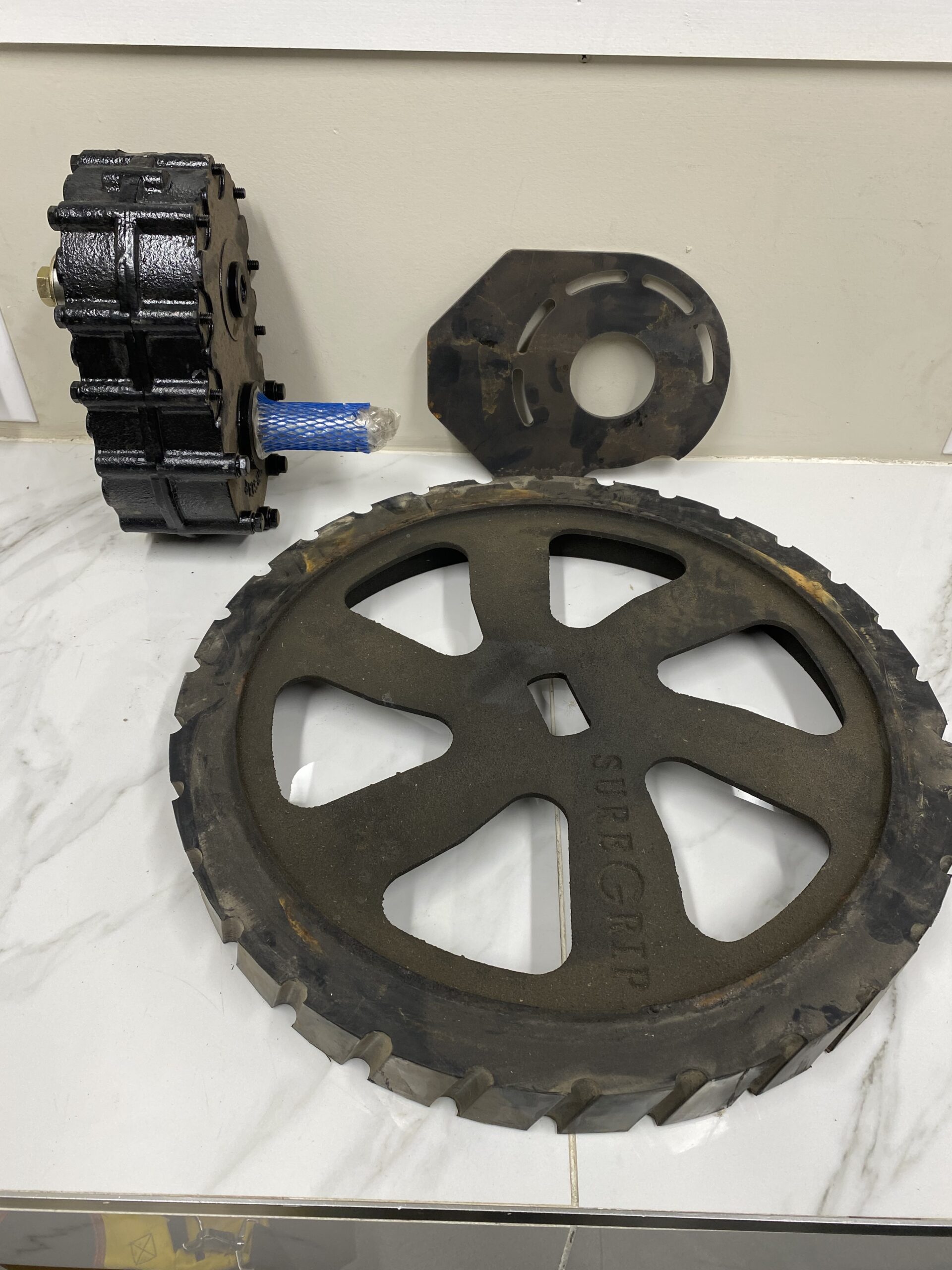 Norstar Sure‑Grip retrofit kit components including a 7‑1/4 inch toothed drive wheel, mounting plate, and drive assembly laid out on a work surface.