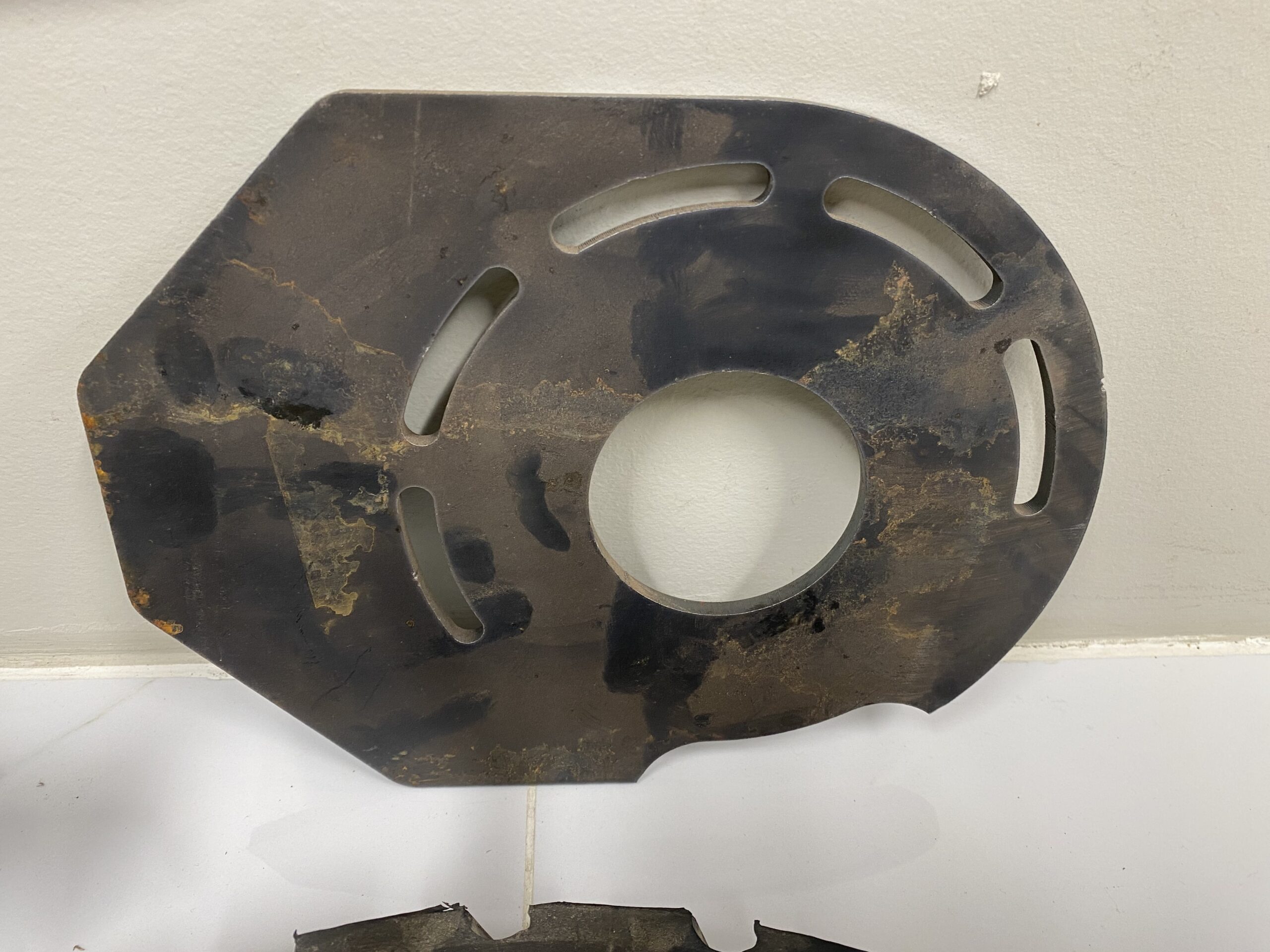 Steel slotted mounting plate from a Norstar Sure‑Grip retrofit kit showing elongated adjustment slots and surface wear.