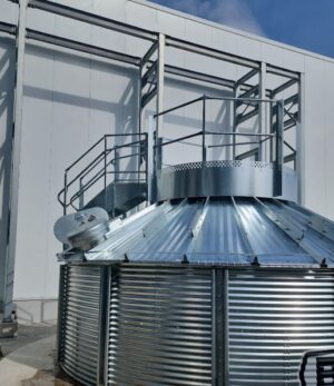 Installed Brock roof stair and fill hole platform with guardrails mounted on the roof of an 18‑foot grain bin.